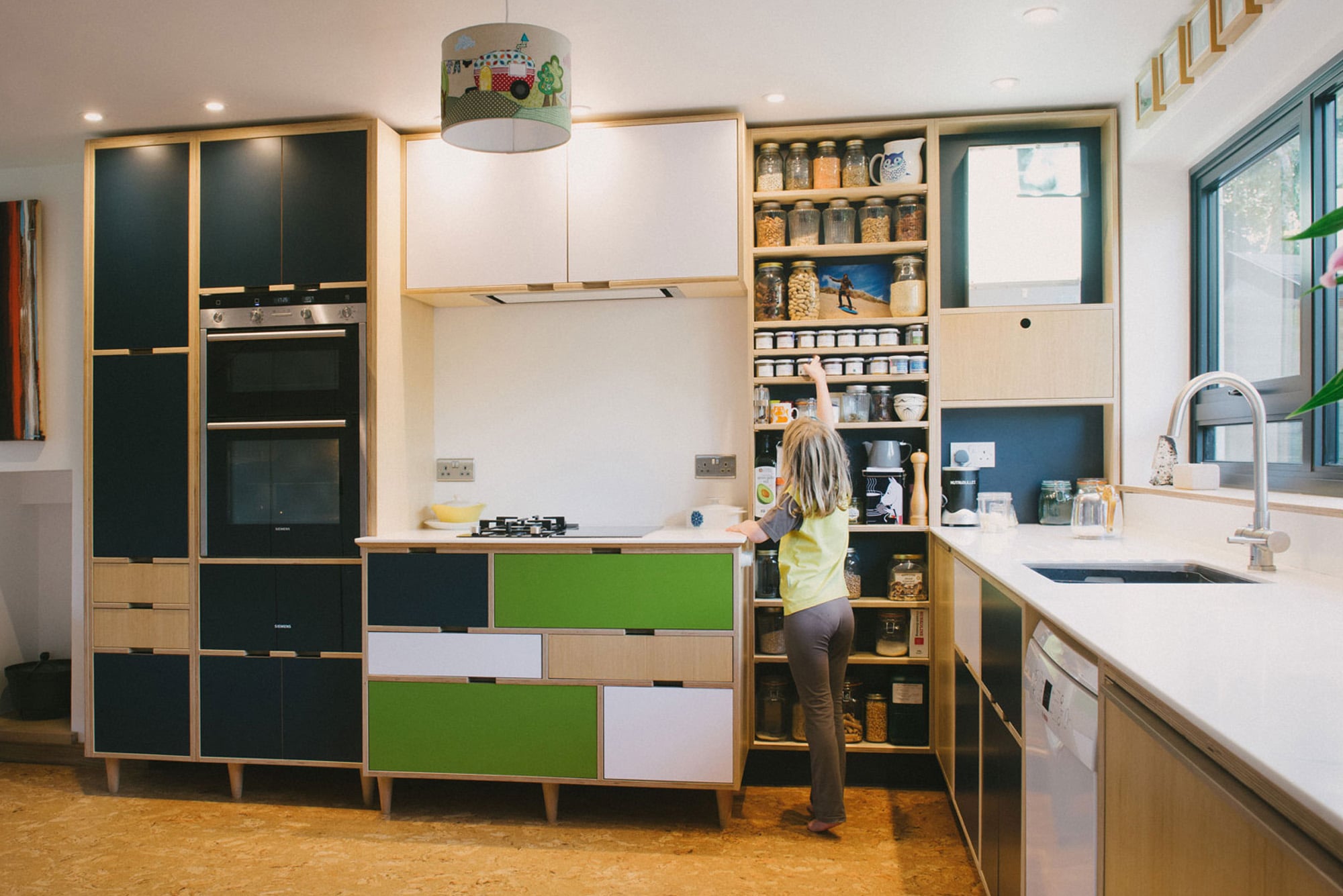 Little girl reaching for spices in green plywood kitchen