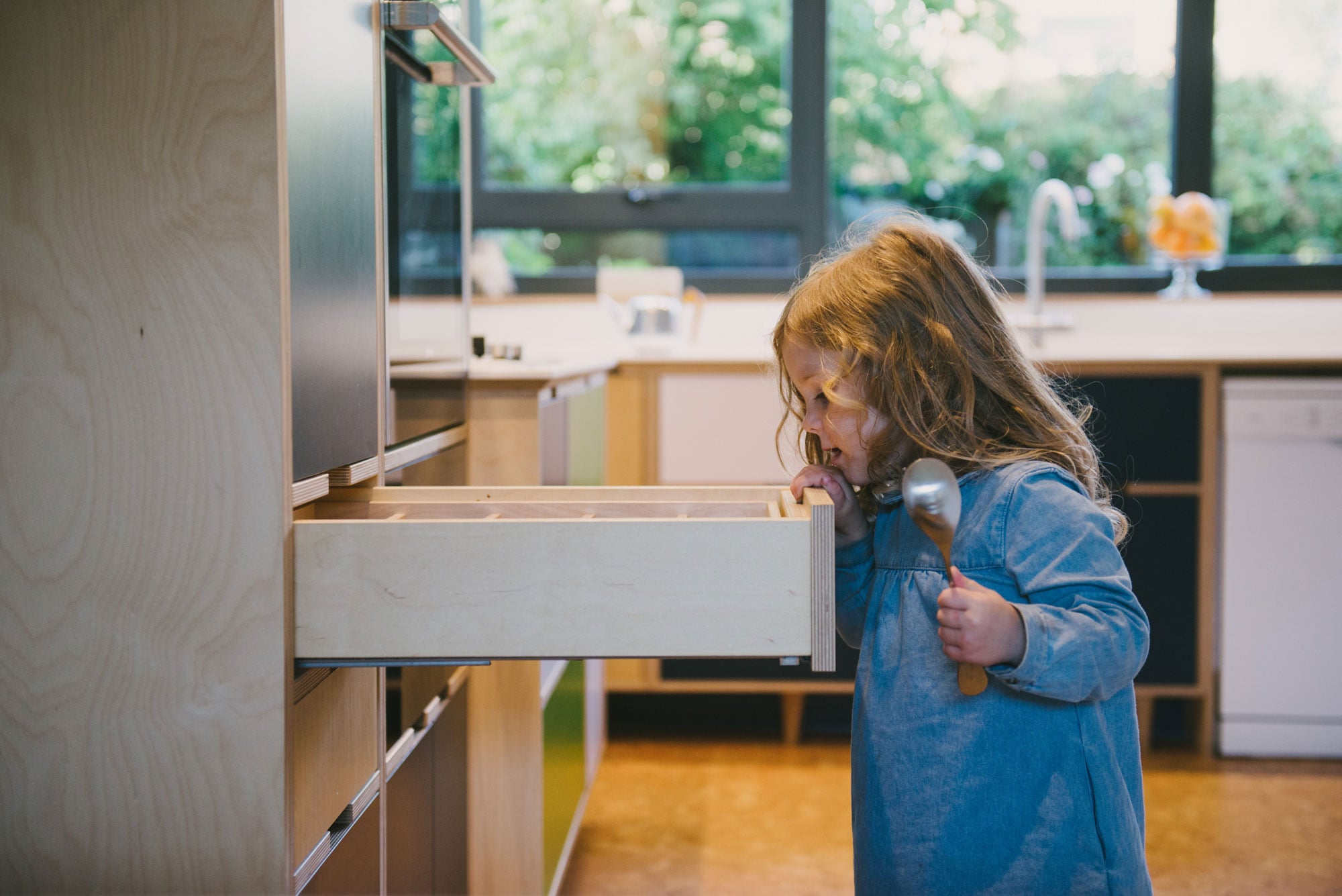 Little girl with spoon looking into plywood drawer