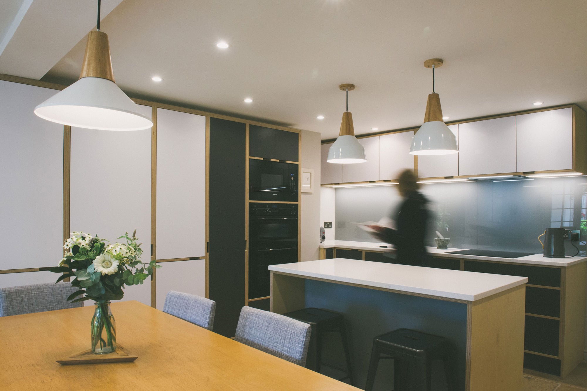 Woman moving across a grey and white plywood kitchen