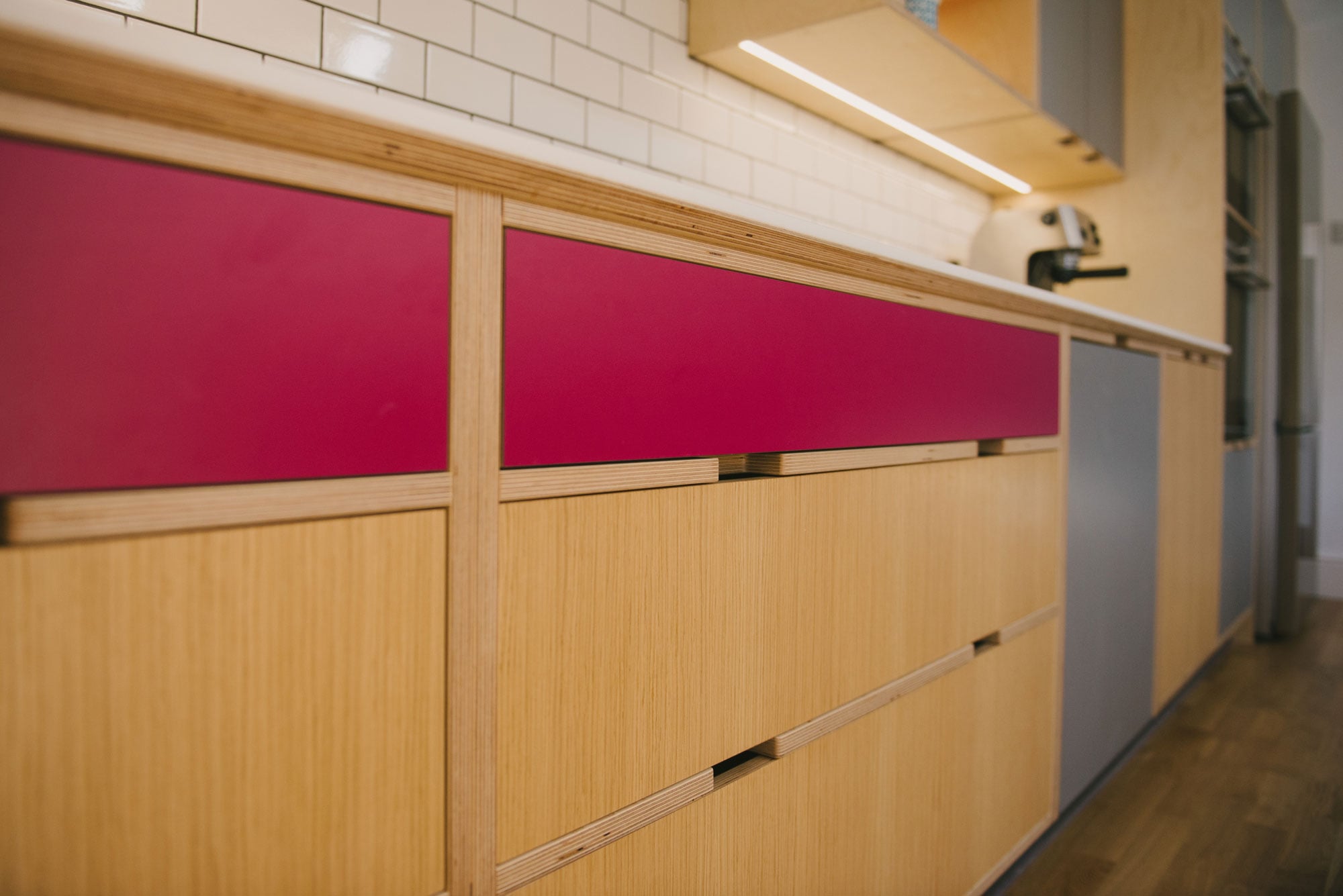 Handleless drawer detail of pink and grey plywood kitchen