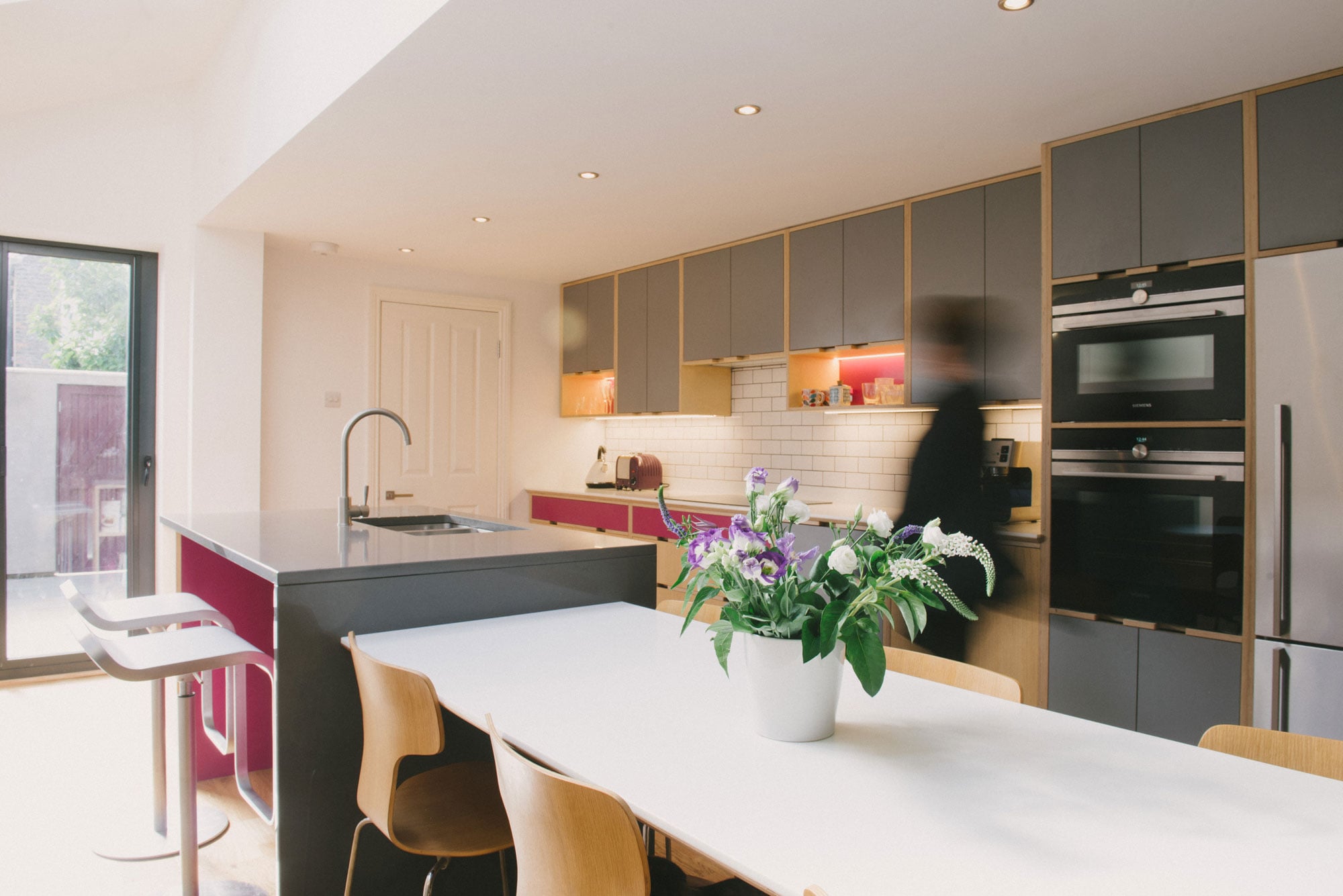 Client walks through their pink and grey plywood kitchen