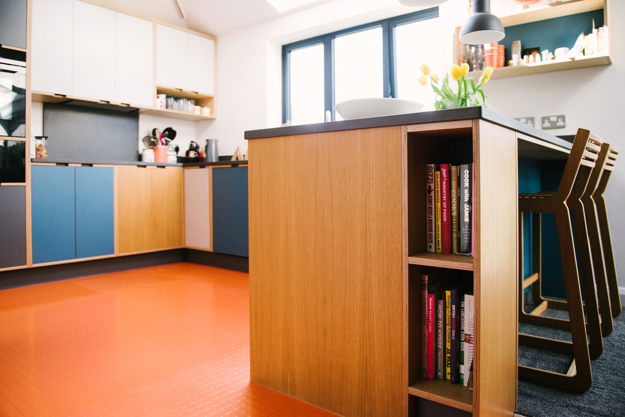 Bookcase in Island of Plywood Kitchen With Orange Floor
