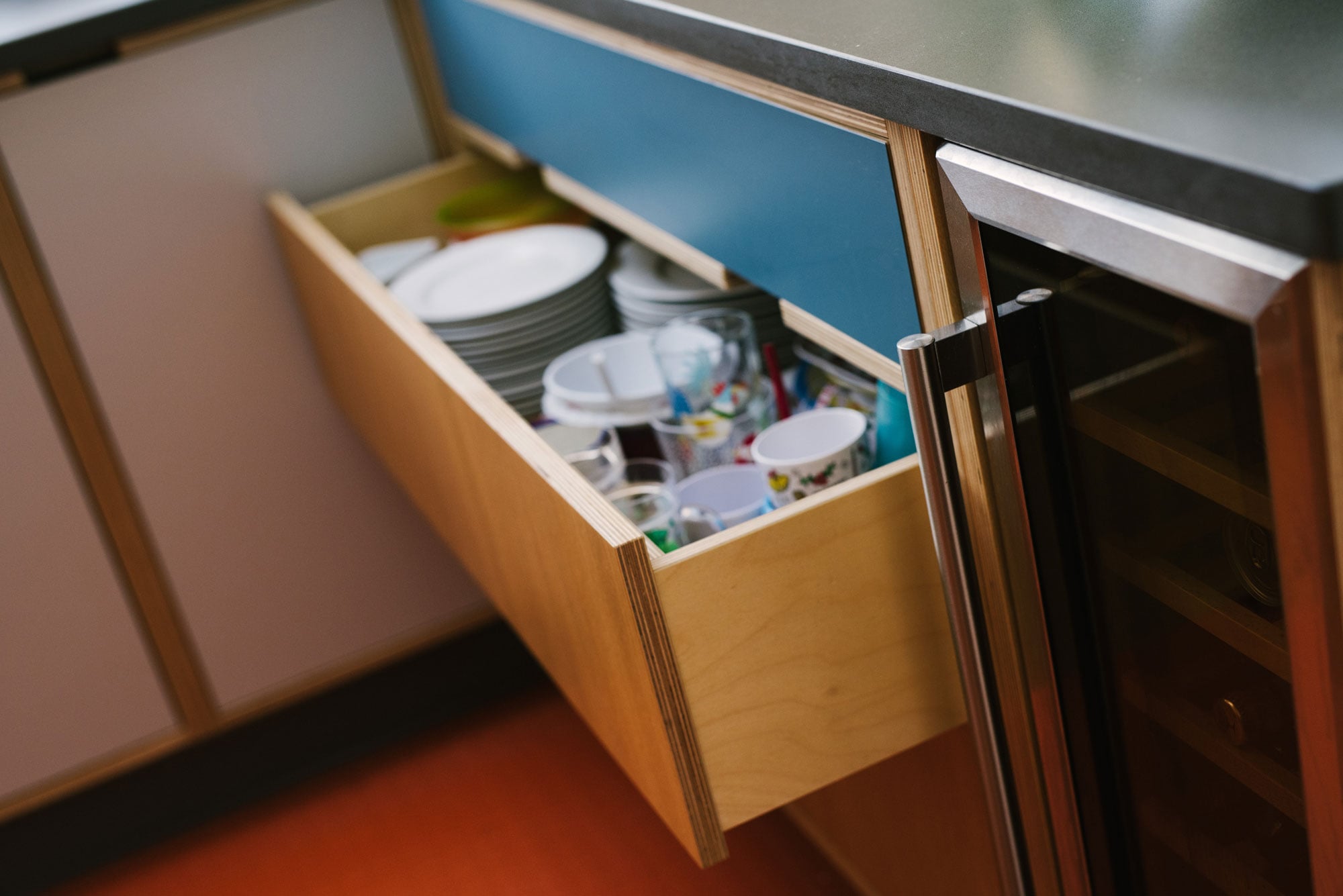 Drawer full of dishes in Plywood Kitchen With Orange Floor