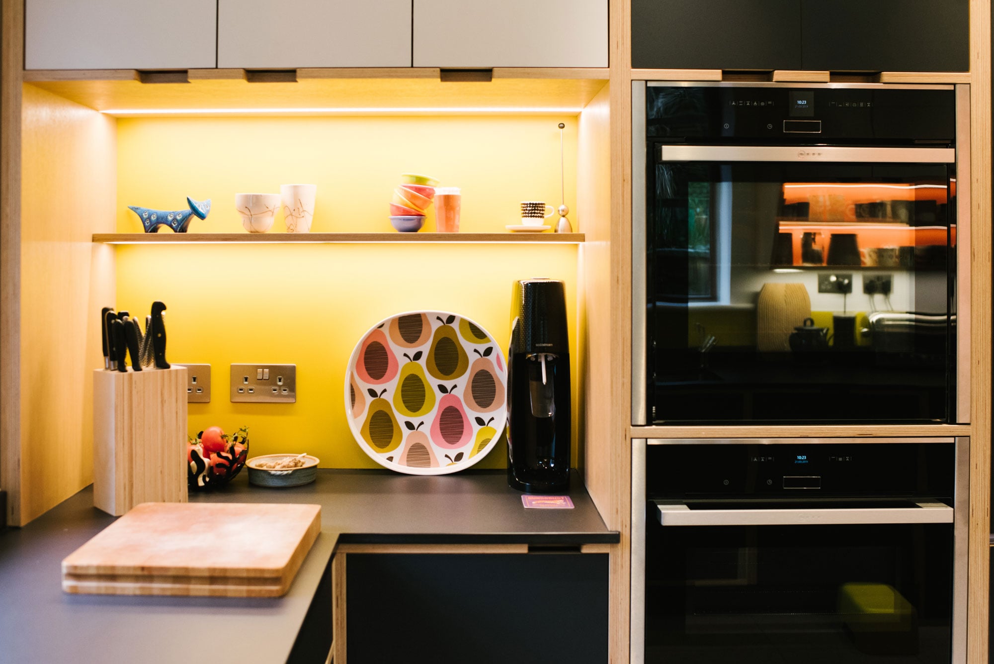 Illuminated Shelving of Black Plywood Kitchen with Yellow Splashback
