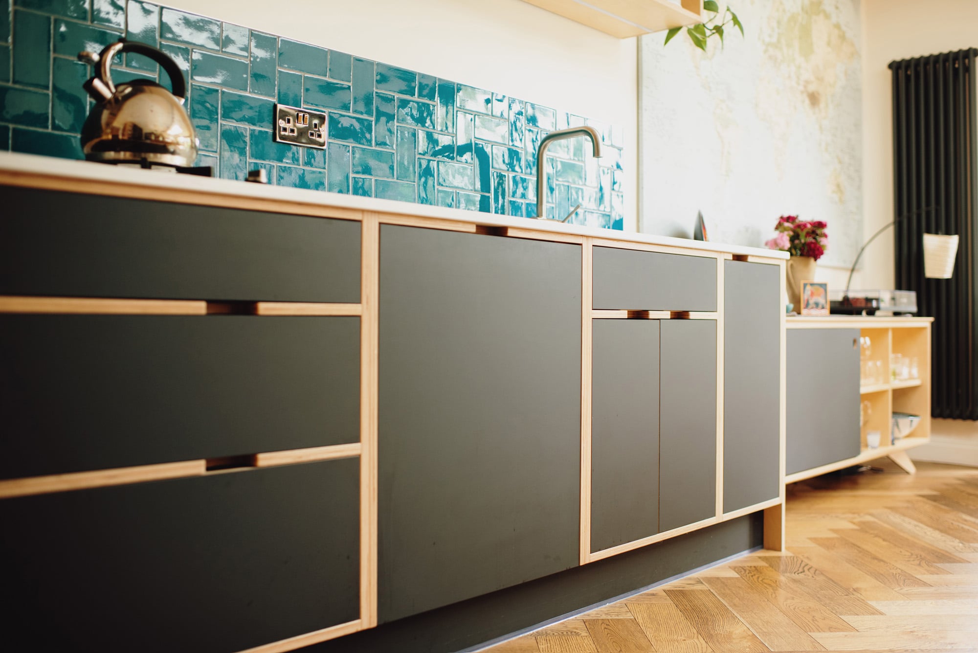 Run of black plywood base units with blue tiles