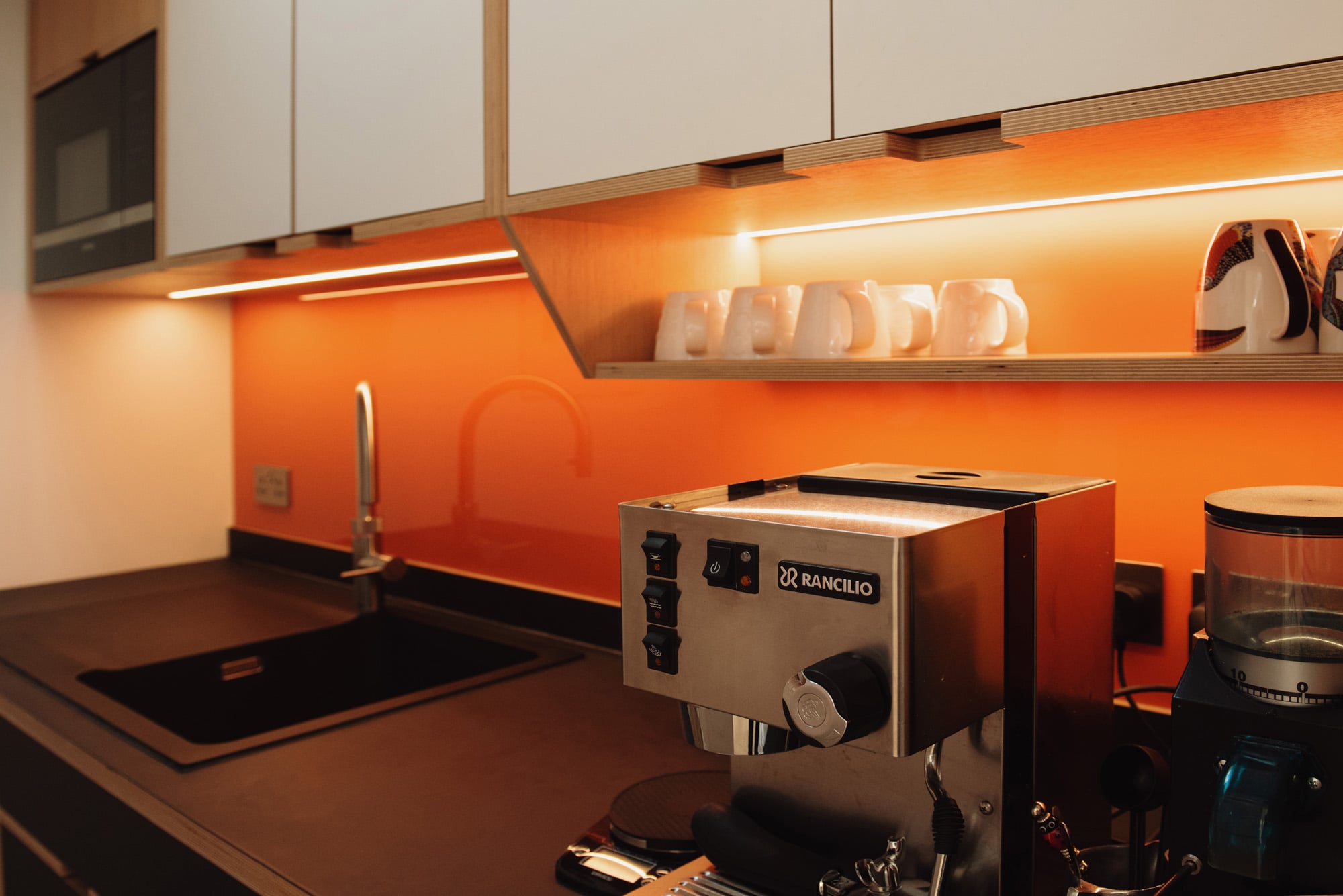 plywood kitchen with orange glass splash back and coffee machine