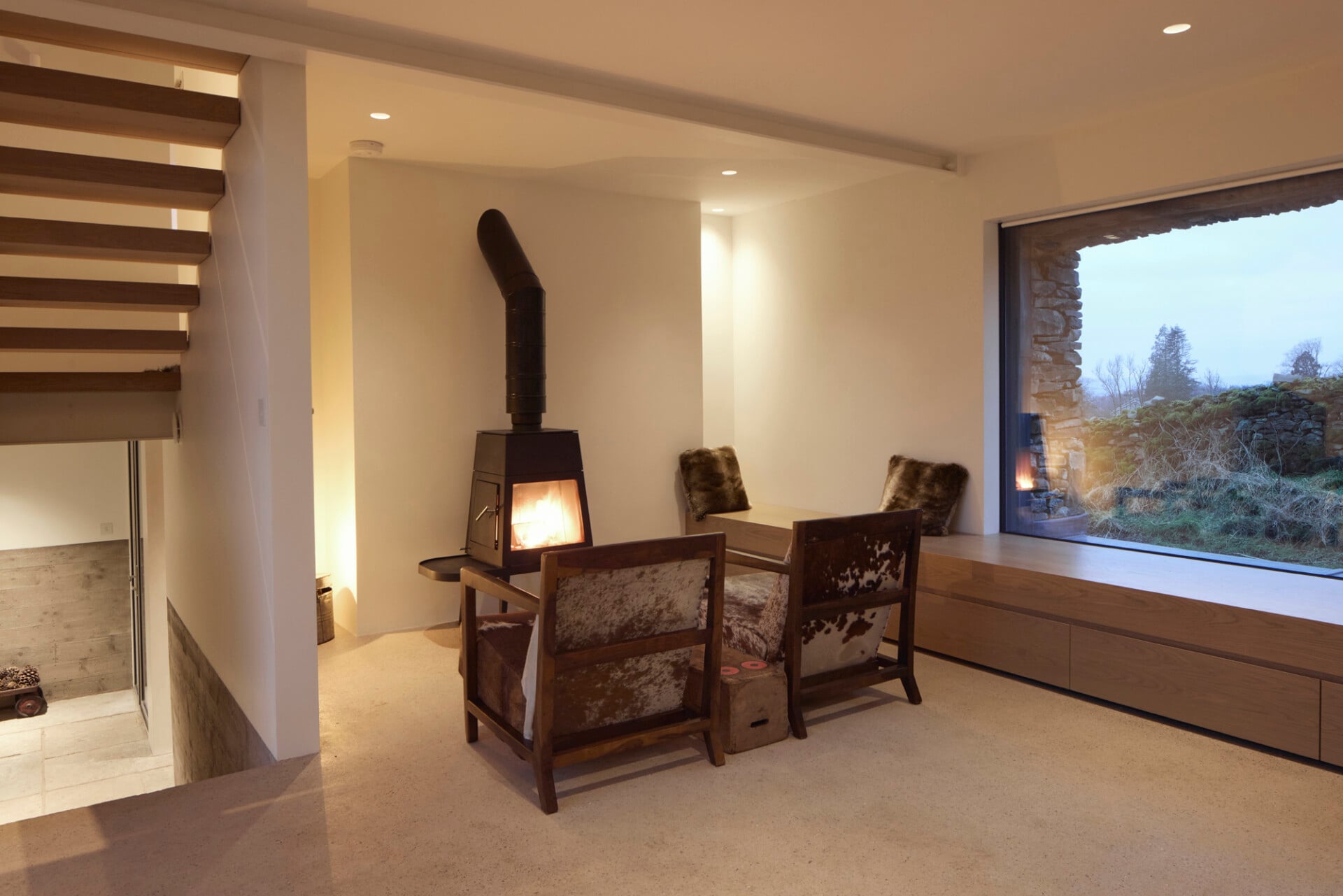Warm living space in barn conversion with log burner, armchairs, and soft uplighting