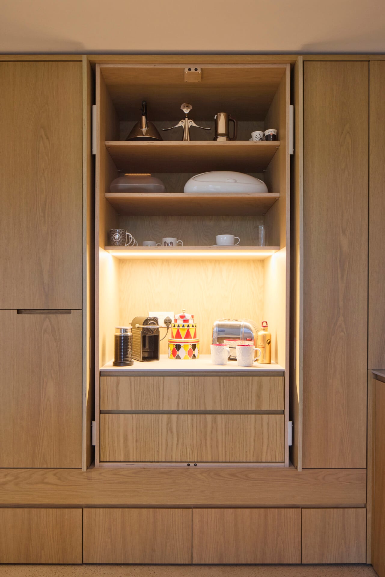 Close-up of open oak pantry with warm lighting and built-in shelving