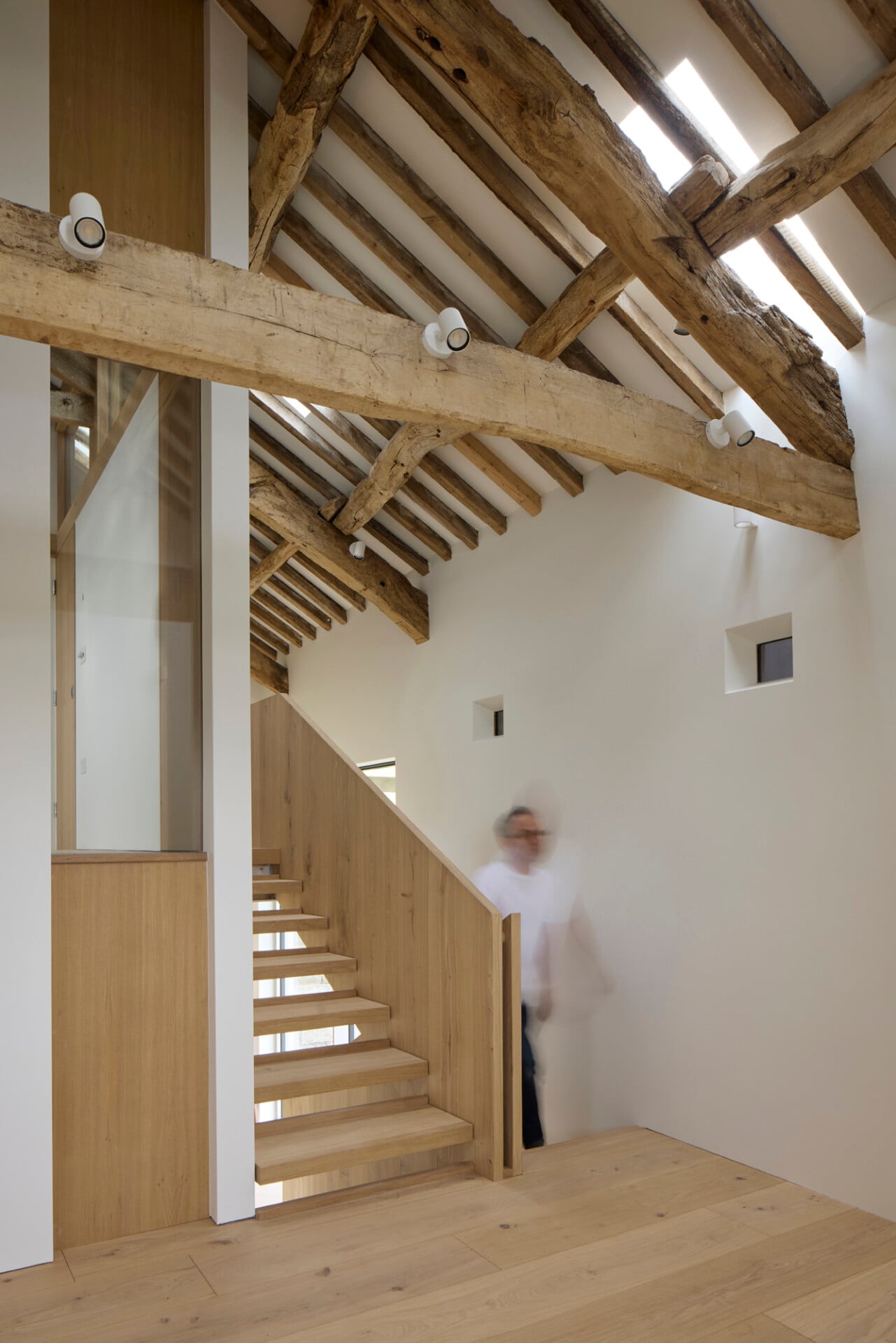 Double-height staircase in barn conversion with open oak treads and timber ceiling beams