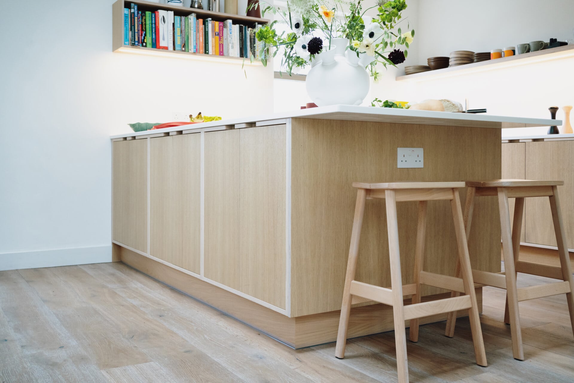Modern oak kitchen with central island, white worktop, and bar stools in bright London home