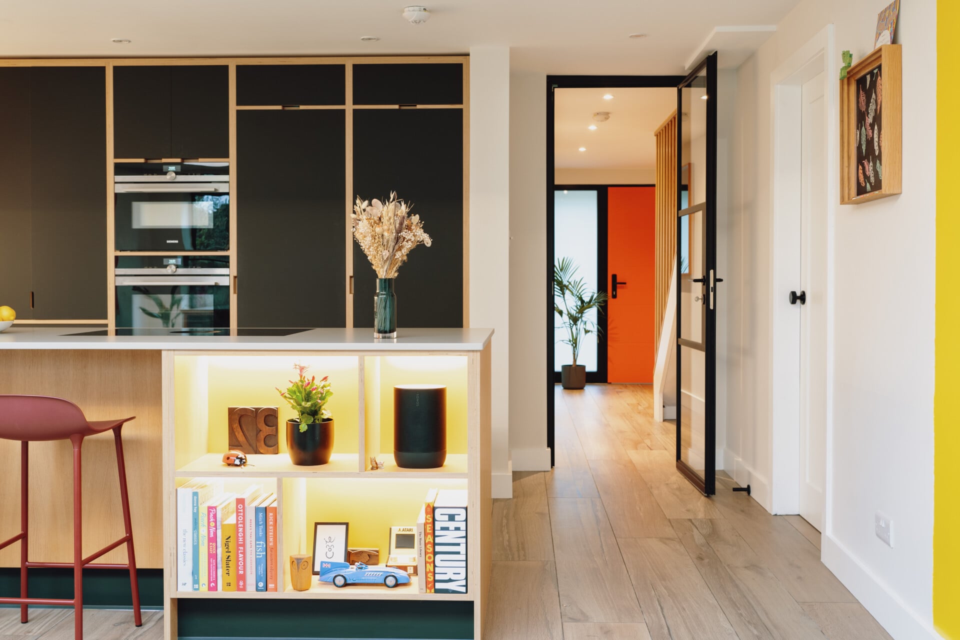 Handleless plywood kitchen with black feature wall, central island, and wood flooring