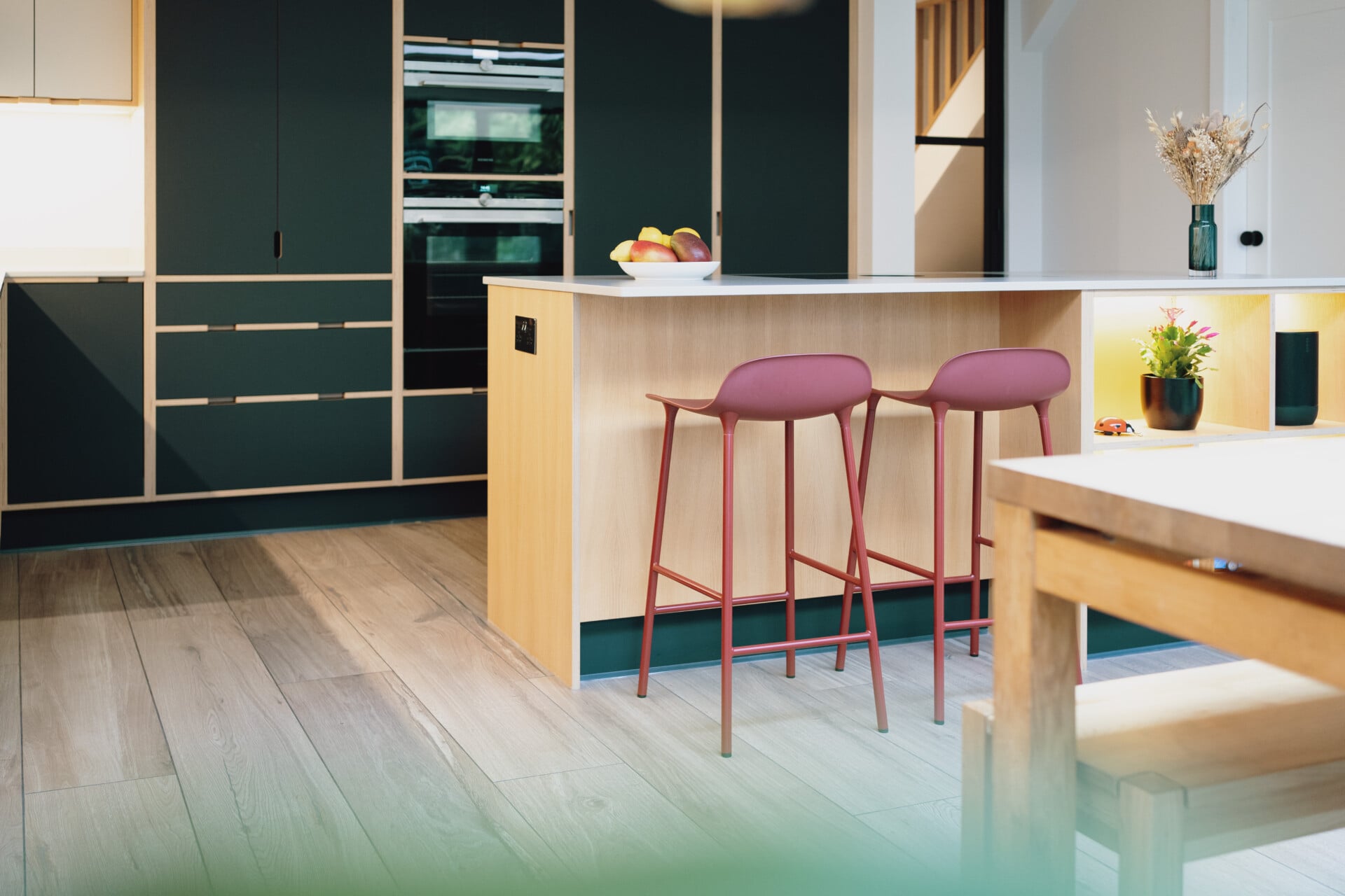 Modern handleless kitchen with red bar stools, black plywood cabinets, and island