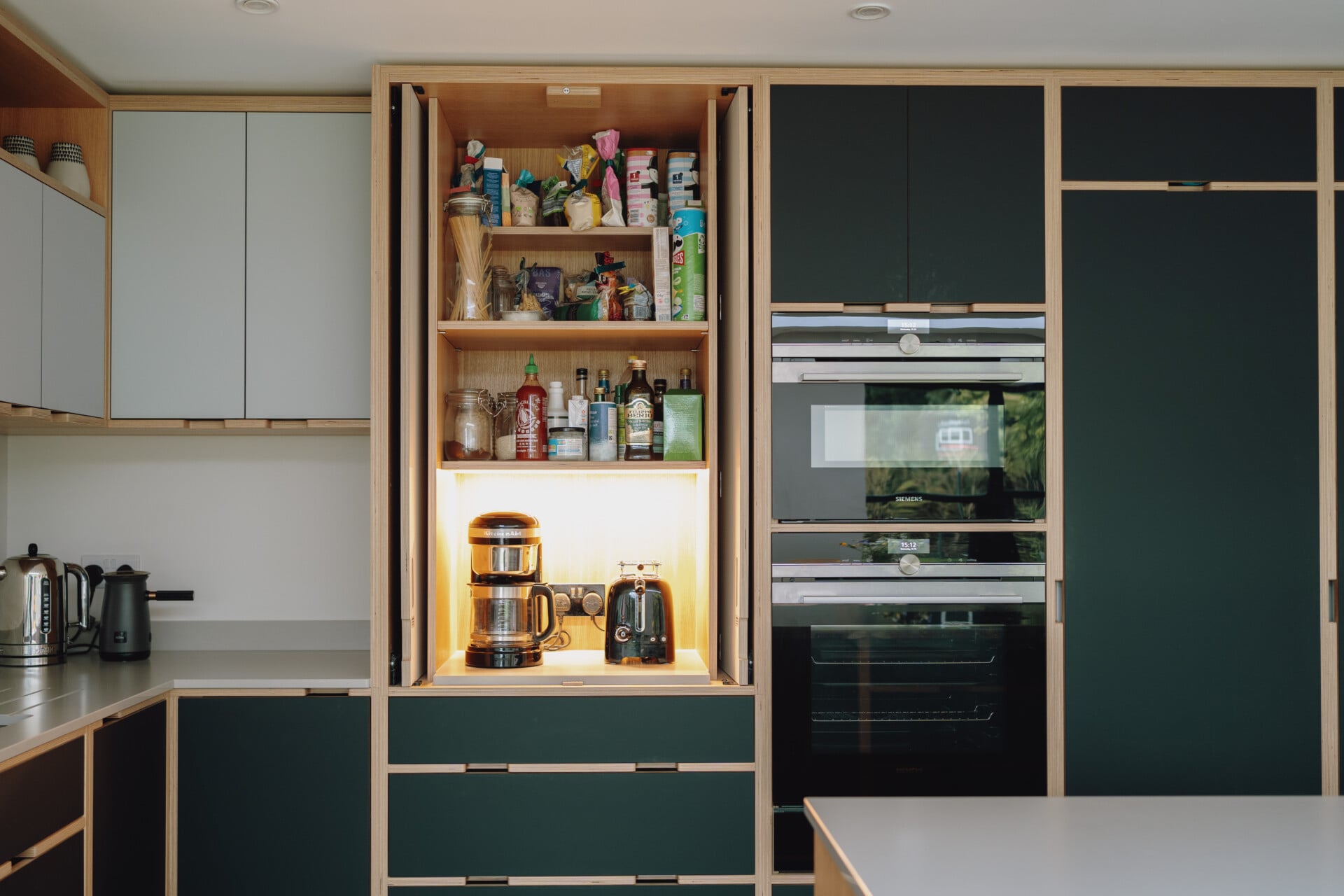 Handleless kitchen with tall pantry storage, black plywood doors, and integrated ovens