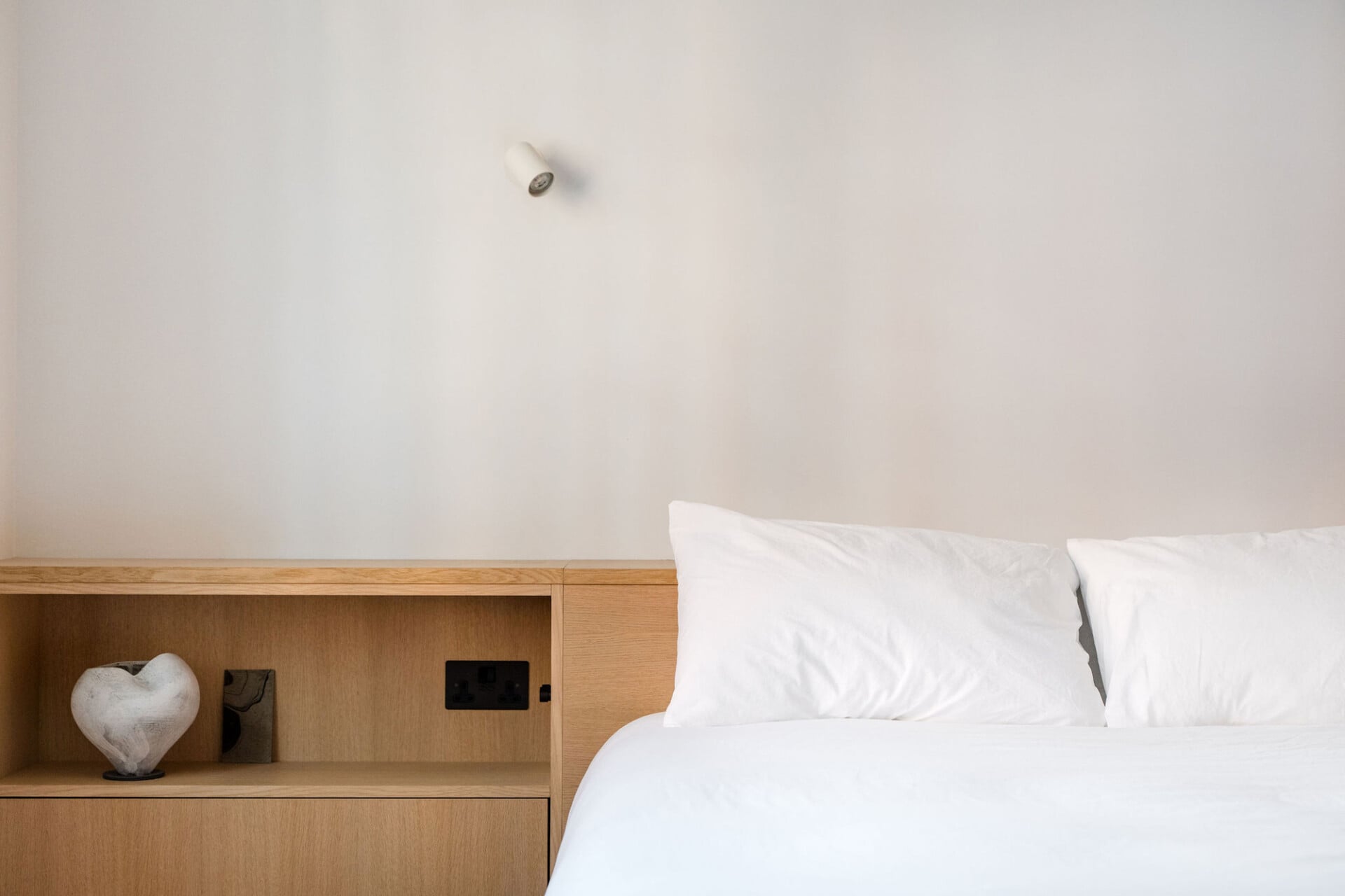 Minimal bedroom with oak headboard, built-in bedside shelf and white walls