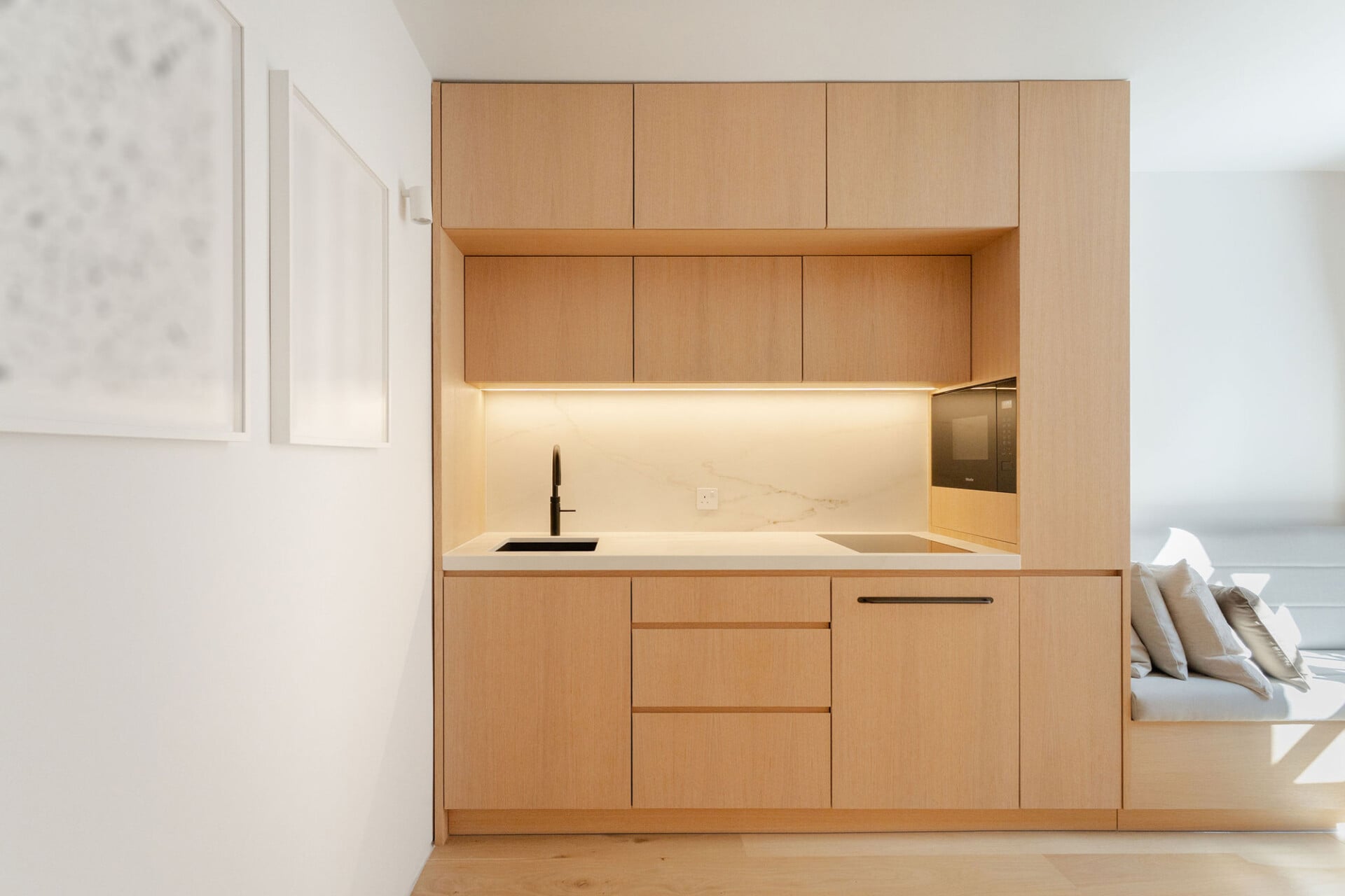 Minimalist plywood kitchenette with oak cabinetry, black tap, and built-in shelves