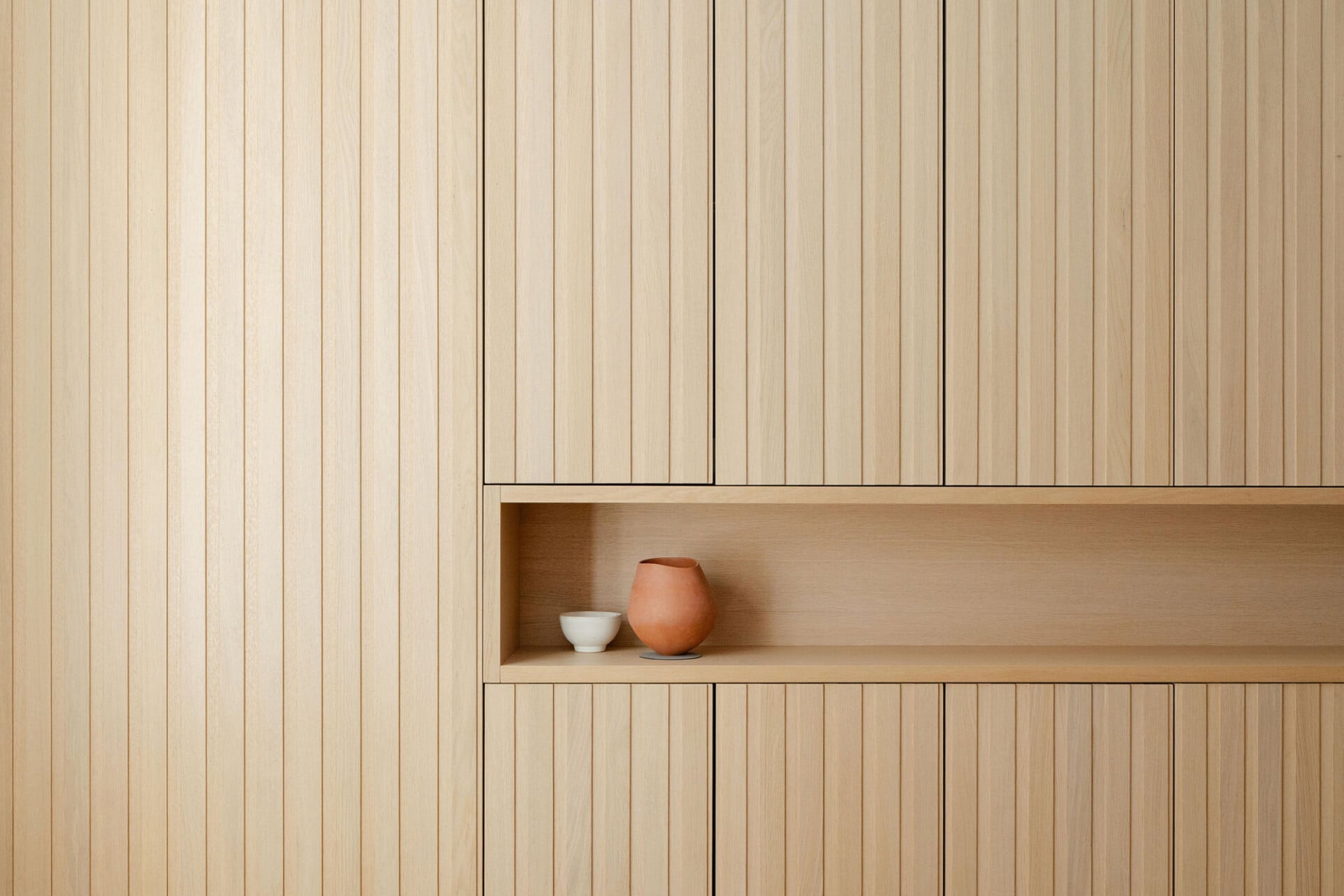 Recessed oak display shelf within a full-height slatted wall