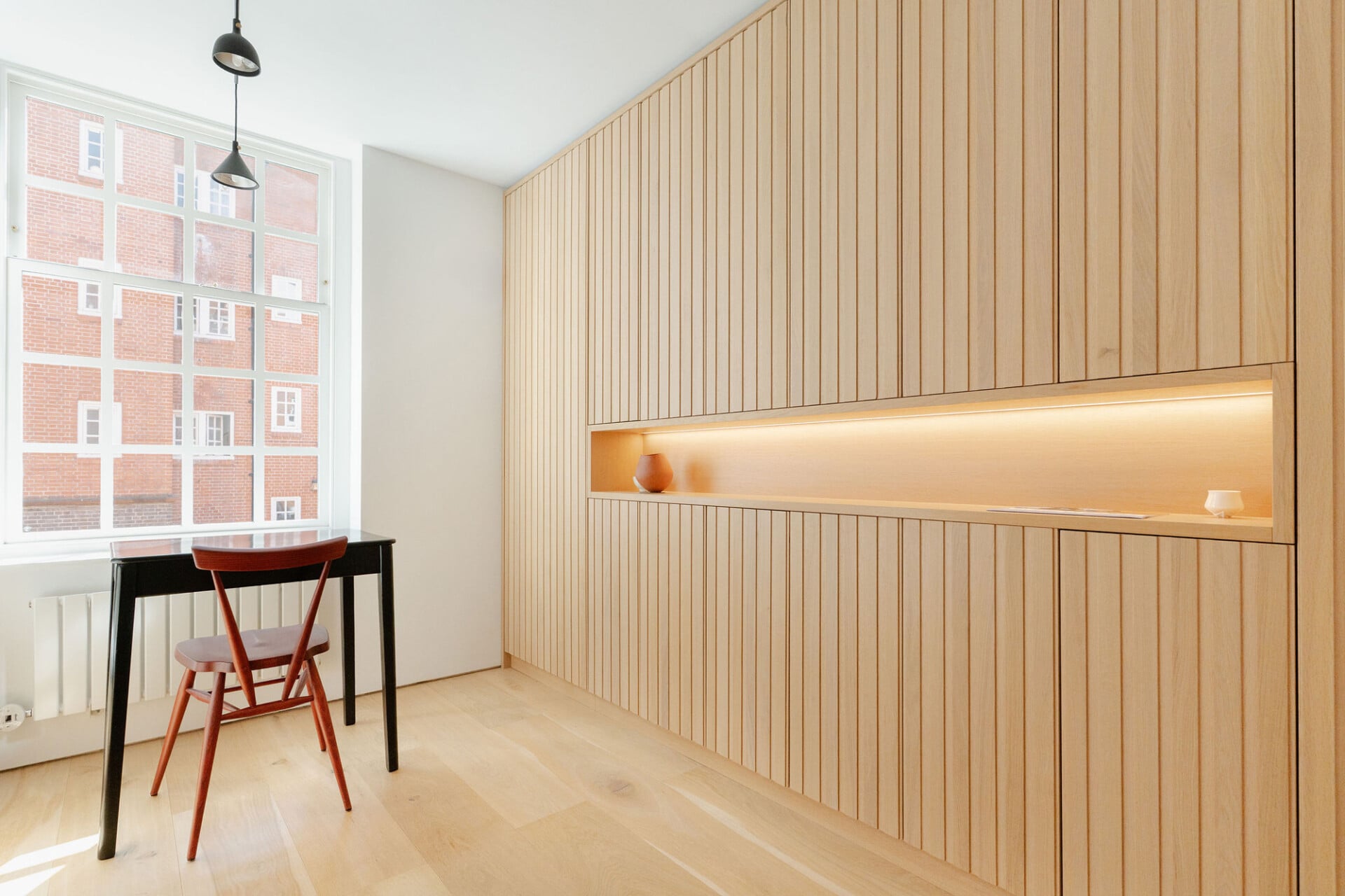 Slatted oak wall with integrated lighting and display shelf in a dining area