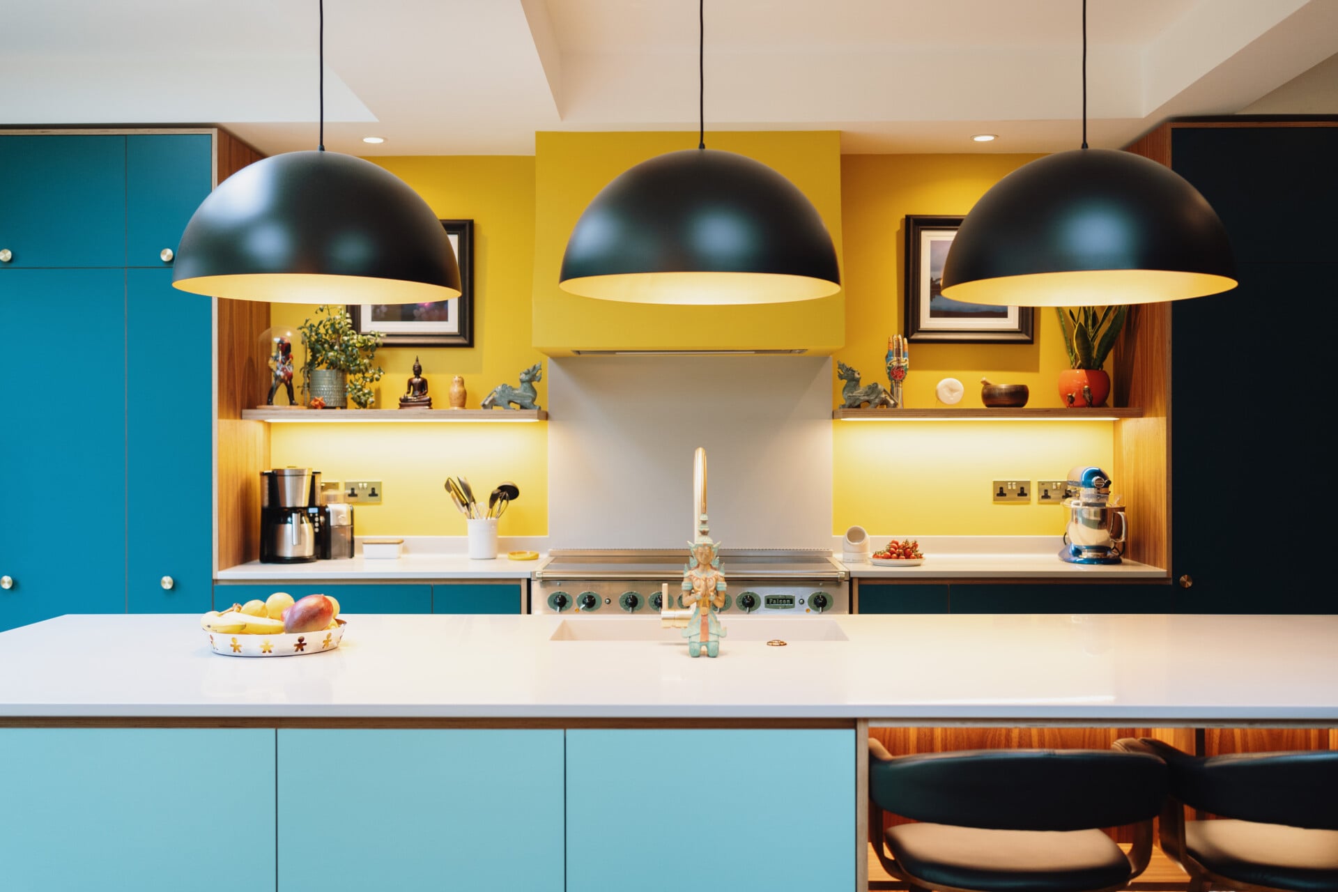 Bright mint green kitchen island with open shelving, teal cupboards, black pendants, and yellow walls