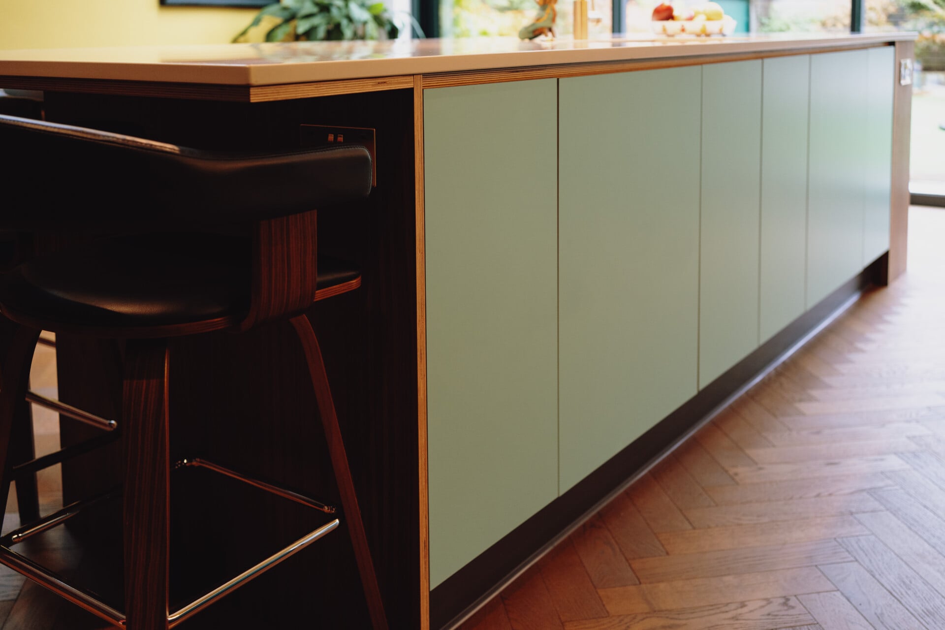 Mint green kitchen island with black plinth and wooden bar overhang