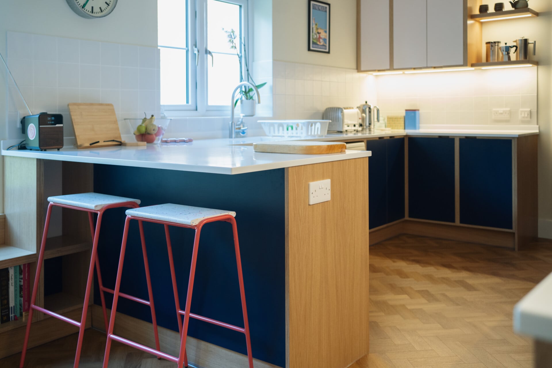 Modern blue kitchen with red barstools, and wood herringbone flooring