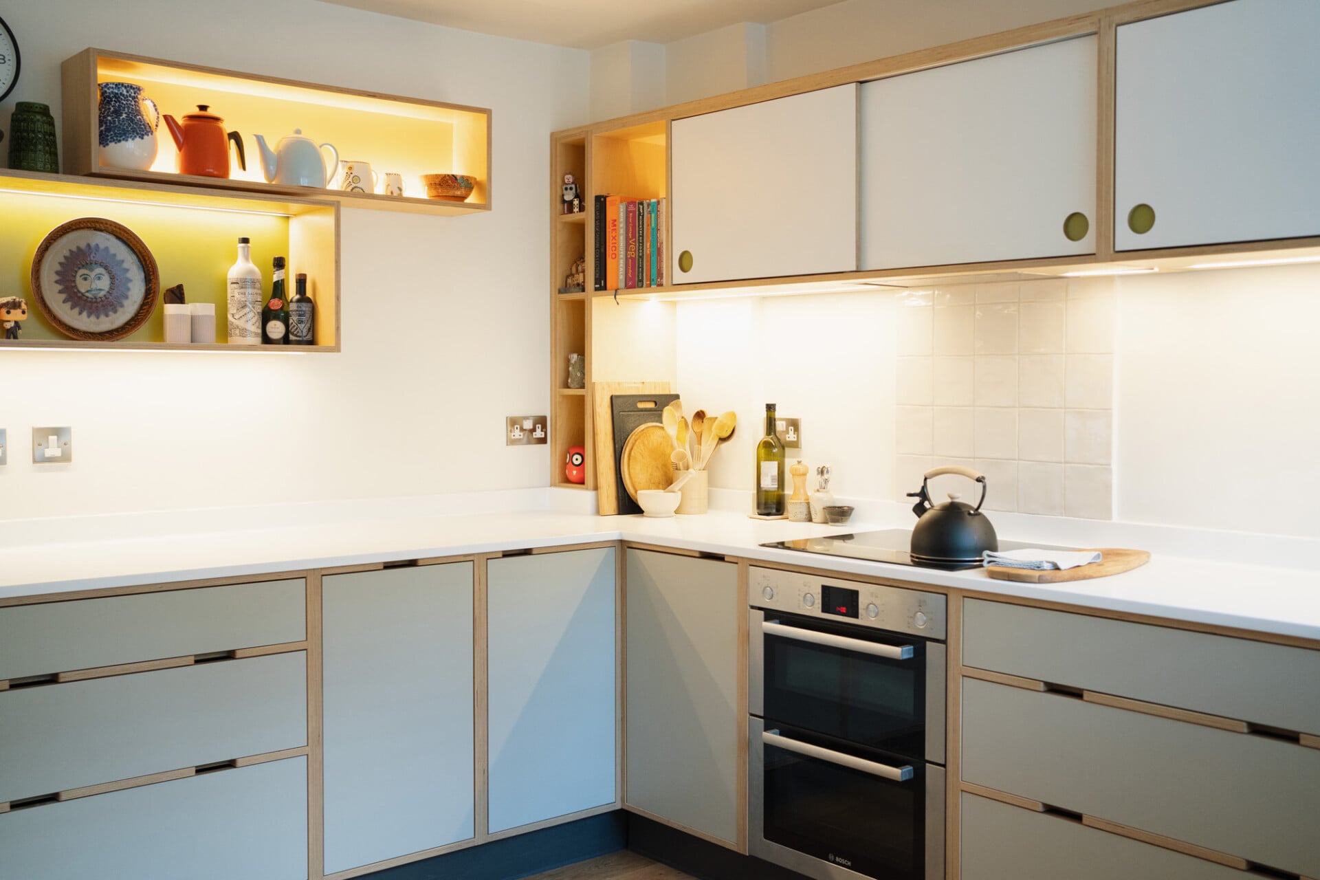 Pale plywood kitchen with corner layout, open shelving, and integrated double oven