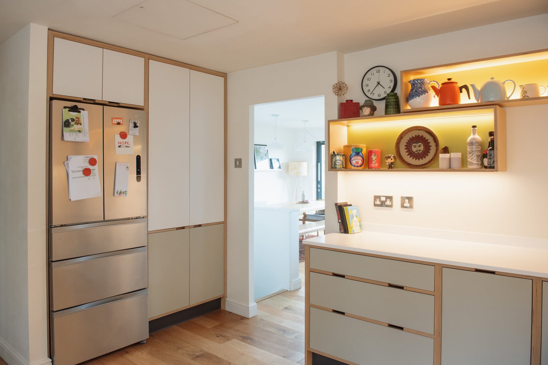 Pale plywood kitchen with tall fridge wall, open shelving, and white cabinets