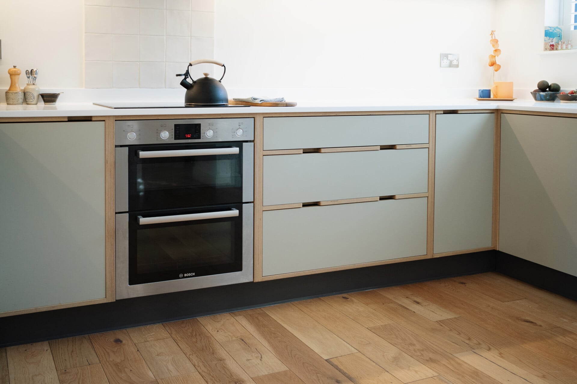 Modern kitchen with pale plywood cabinets, double oven, and white worktop