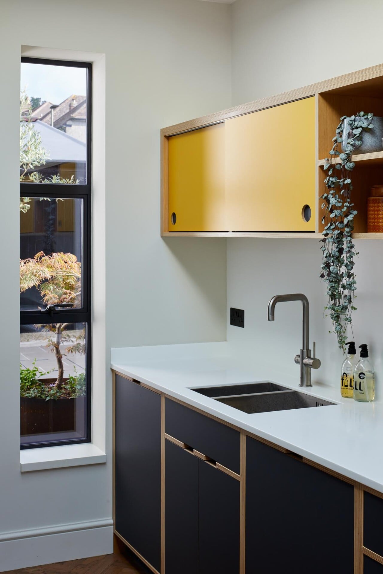 Compact plywood kitchen in London with modern yellow cabinets, skylight, and garden view