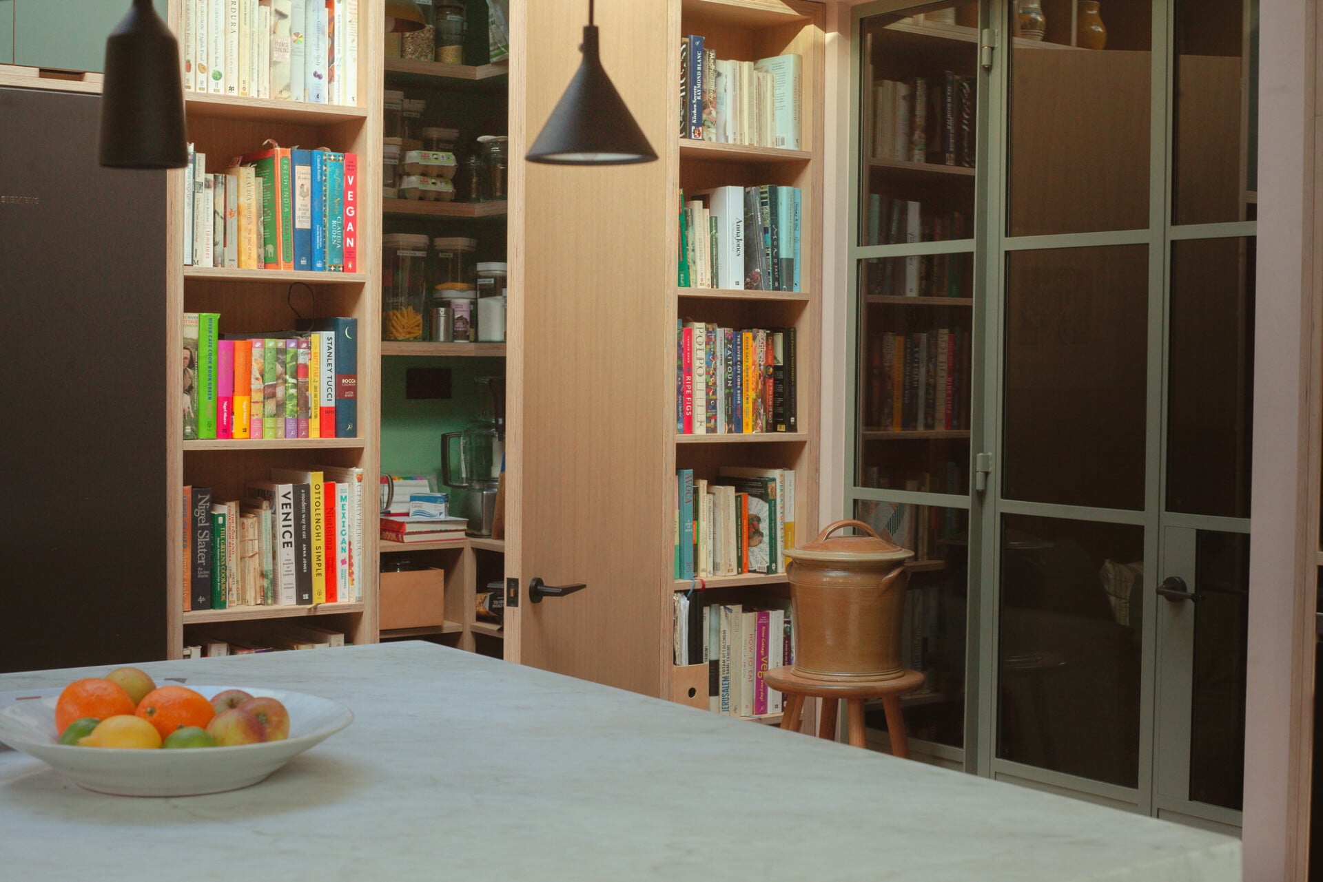 Open-plan kitchen-diner in London with large island, pendant lights, and floor-to-ceiling bookcase