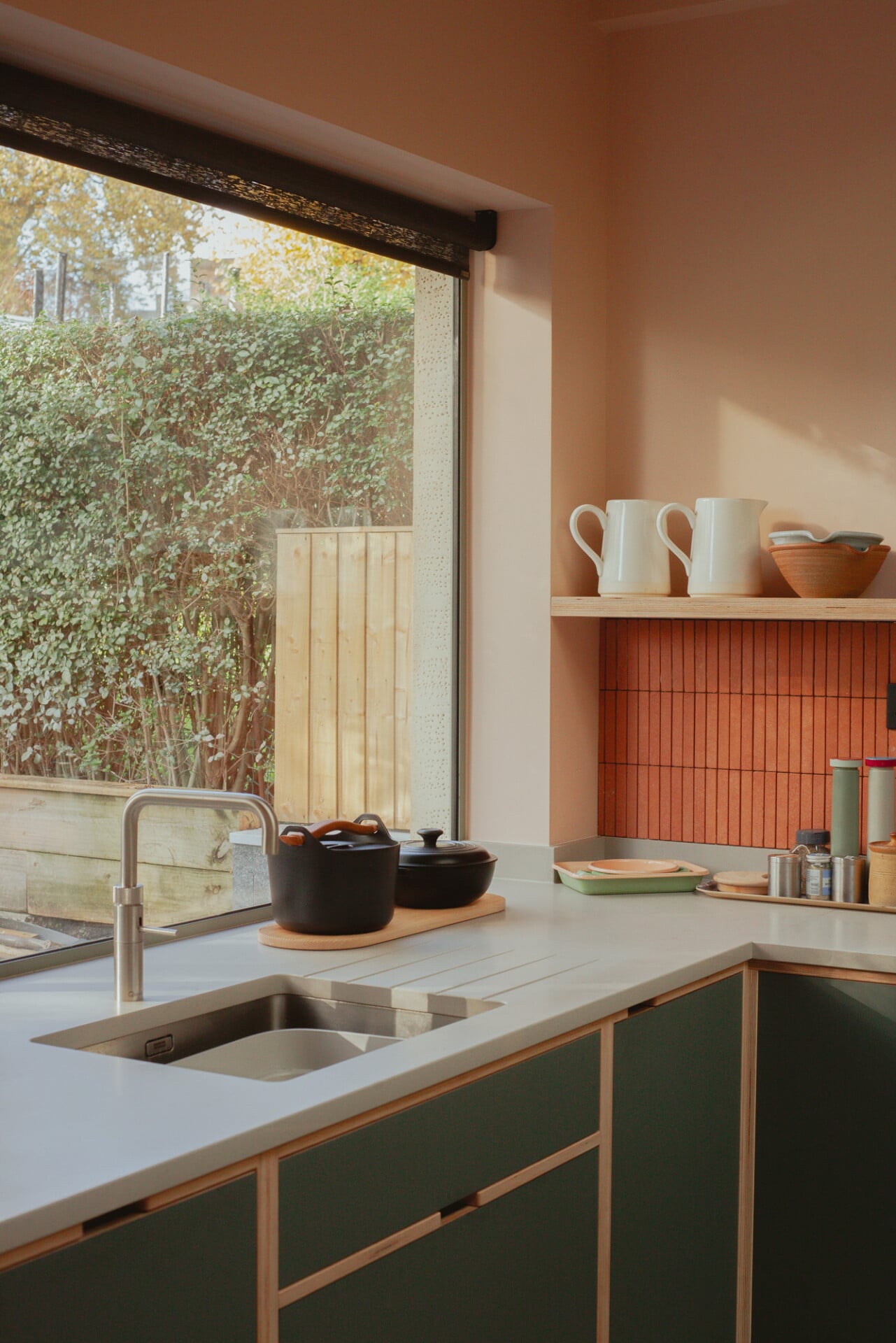 Stylish London kitchen with pink walls, green cabinets, and garden view