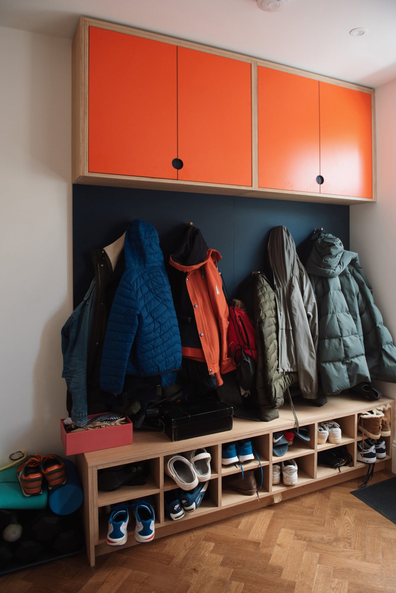 Family-friendly mudroom with coat storage and orange cabinets in vibrant London home