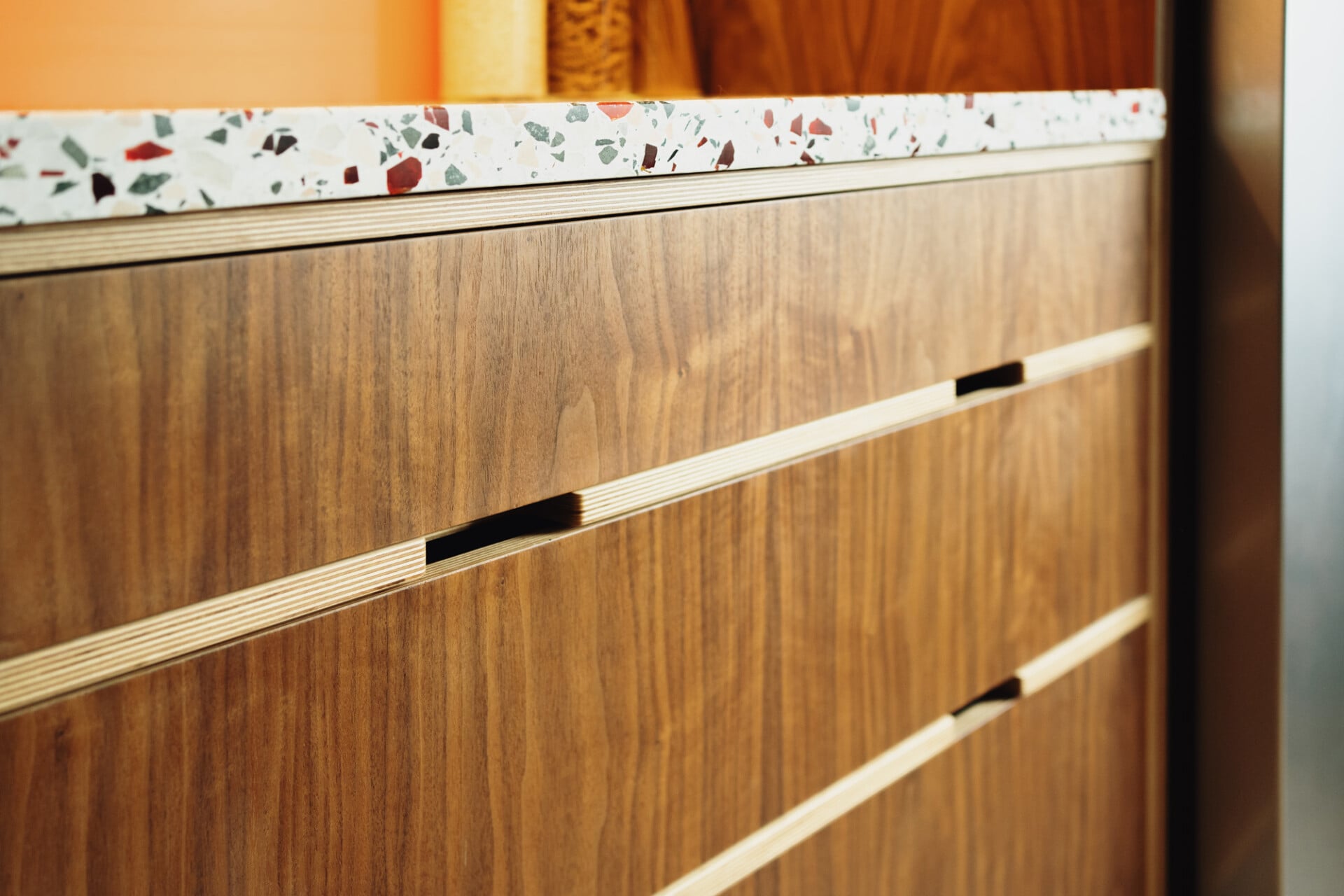 Close-up of walnut plywood handleless drawers with terrazzo worktop