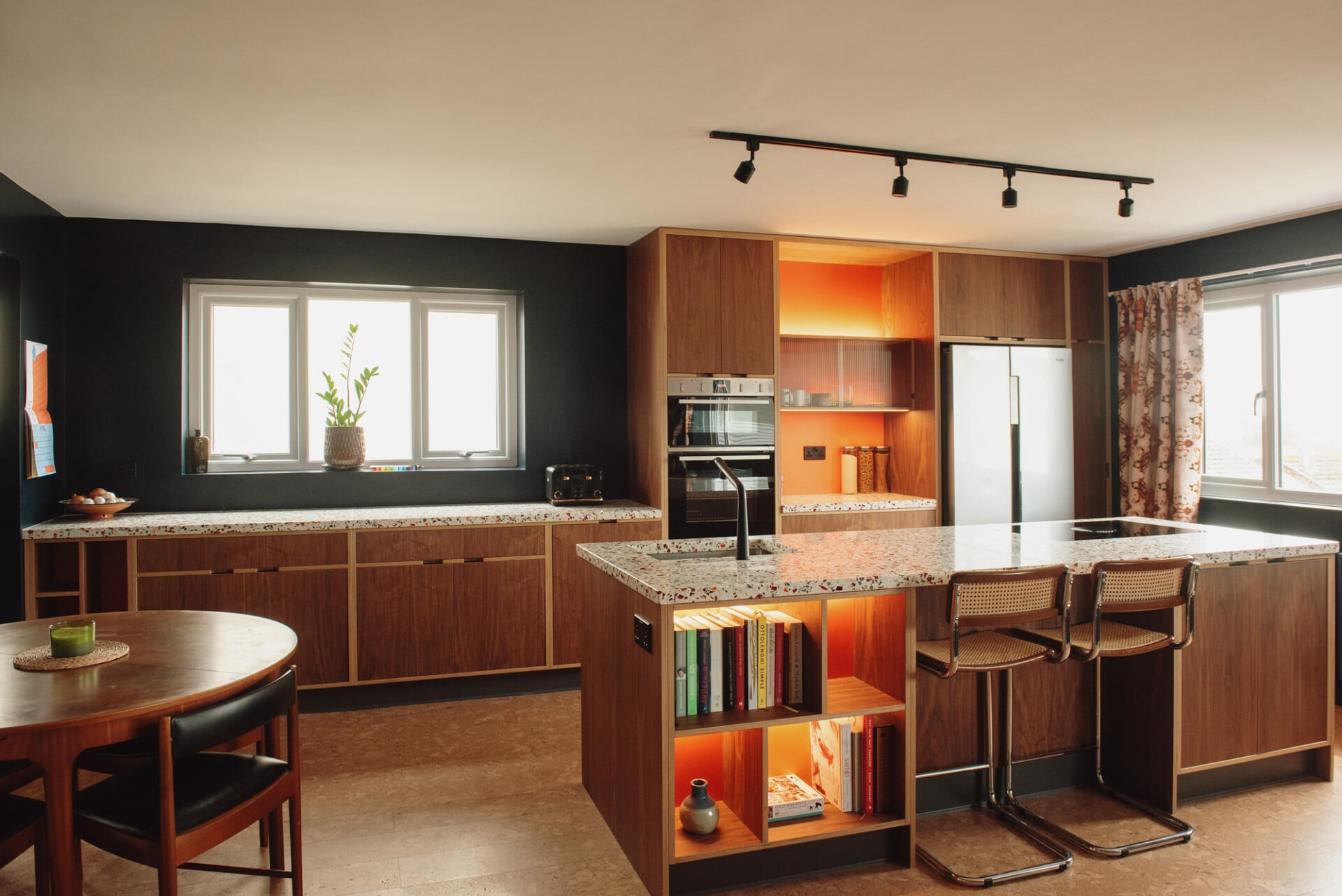 Open-plan walnut plywood kitchen with bar seating and black feature wall