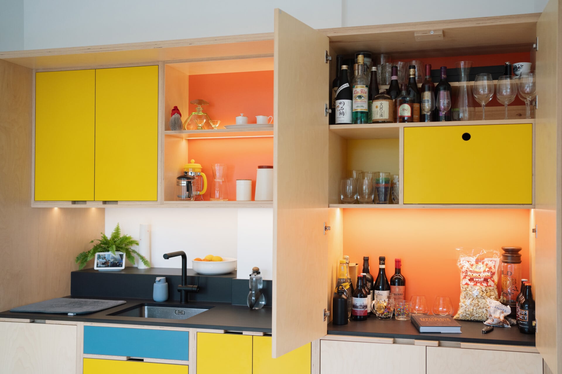 Yellow plywood kitchen with built-in drinks cabinet, orange splashback, and modern sink