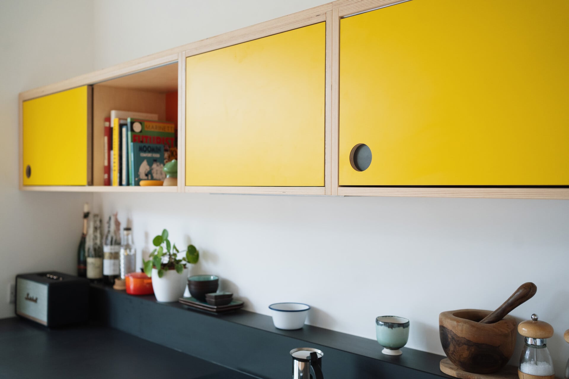 Minimalist kitchen with yellow plywood cabinets and black countertop in modern London home