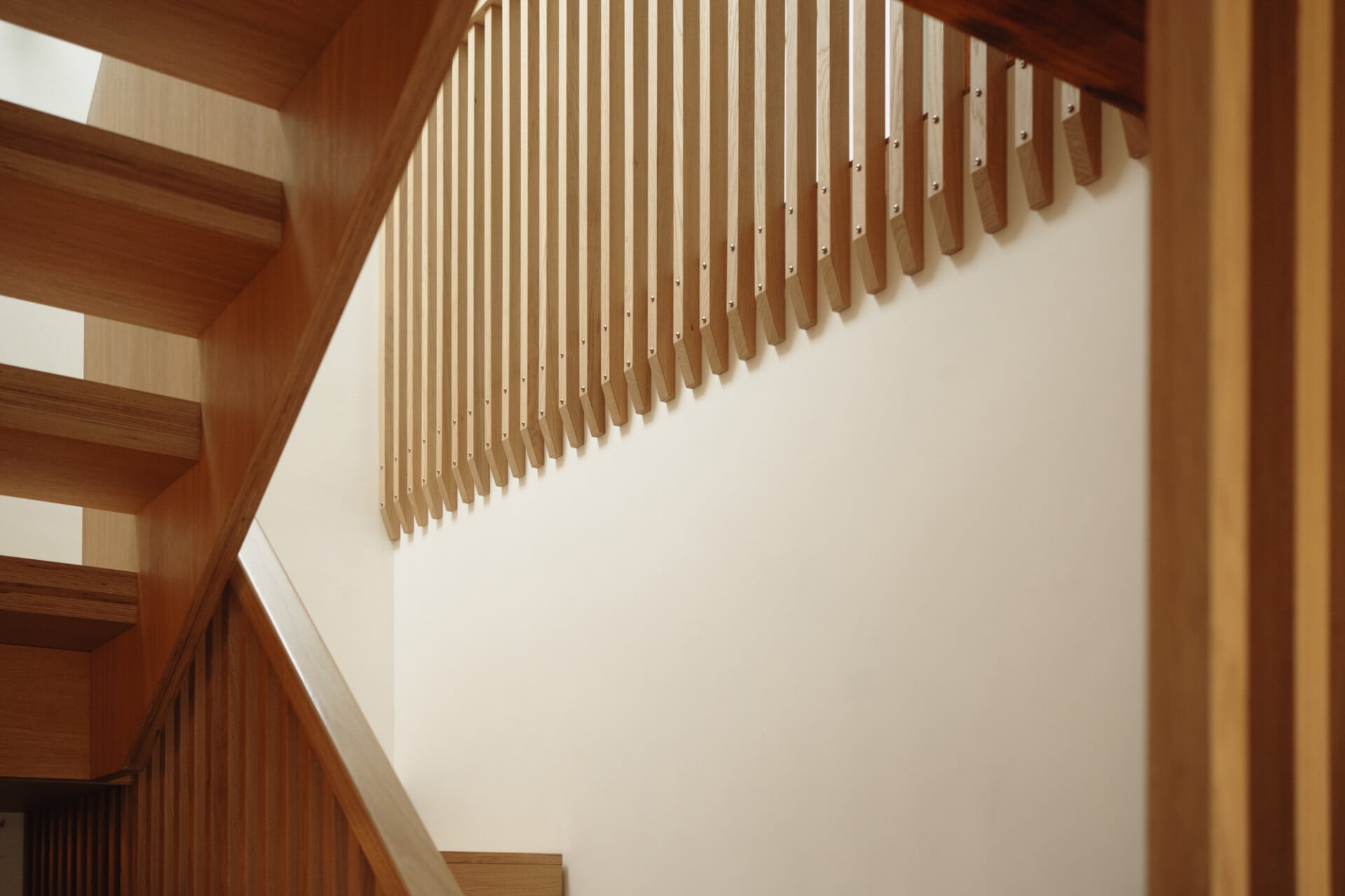 Detail of timber stair rail with vertical slats and white plaster wall