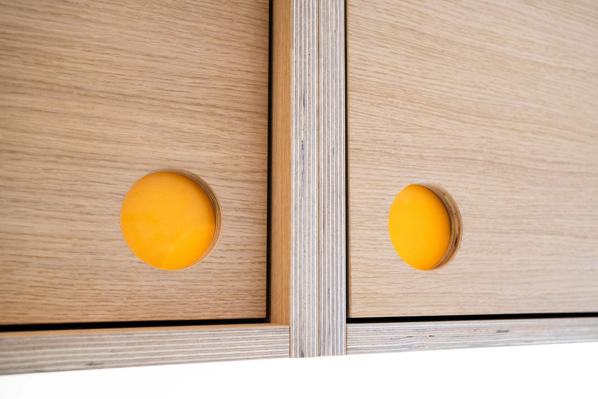 Close-up of yellow plywood door fronts with circular finger pull detail